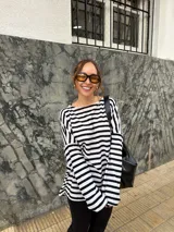 Conjunto compuesto por remera de manga larga oversize a rayas horizontales blancas y negras con escote bote, y pantalón negro de corte flared.