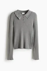 Buzo tipo polo de punto acanalado color gris, con cuello clásico, tapeta con tres botones nacarados y terminaciones con ribetes sobrehilados en puños y ruedo.