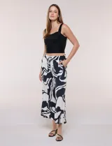 Pantalón ancho negro y blanco con estampado abstracto, cintura elástica con cordón ajustable, bolsillos delanteros con detalles de pompones y corte tobillero.