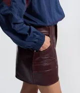 Short pollera de tiro medio confeccionado en poliuretano con acabado símil cuero. Presenta diseño de corte recto, cierre frontal con cremallera, trabillas para cinturón y dos bolsillos delanteros con solapa.