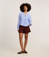 Blusa tipo bata de color celeste con mangas largas y cuello mao con lazo. Presenta detalles de bordado floral calado tipo laise en el frente y cierre parcial con botones.