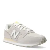 Championes New Balance modelo 373 para mujer, color gris claro y beige, con detalles en blanco y cordones blancos. Presentan una combinación de gamuza y malla.