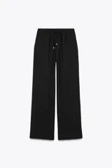 Pantalón negro de tiro alto con cintura elástica ajustable mediante cordones con terminales dorados. Presenta pernera ancha y bolsillos laterales. La tela tiene una textura sutilmente arrugada o plisada.