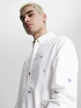 Camisa blanca de popelina de puro algodón con estampado de banderas náuticas y logos de Tommy Jeans bordados. Corte clásico, cuello abotonado, puños con botón y bajo redondeado.