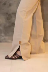 Pantalón vaquero de tiro alto y corte recto en color beige. Presenta tajos laterales en el bajo con detalles en cuero y terminación deshilachada. Incluye botón de guampa y detalle de pespuntes en los bolsillos traseros.