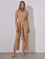 Mono color beige de crepe, marca Sharagano. Escote en V cruzado, sin mangas, con cintura elastizada y lazo de ajuste. Abertura central en espalda con cierre invisible y doble abotonadura. Bolsillos inclinados en delantera con aplique de botones.