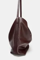 Bolso formato saca color marrón oscuro, confeccionado en piel. Tiene doble compartimento interior, asa de hombro y bolsillo interior con cierre mediante cremallera.