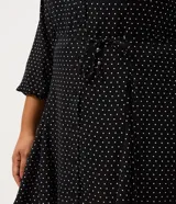 Vestido corto tipo chemise de poliéster con estampado de lunares, cuello camisero con botones frontales, mangas largas con puños elásticos y lazo ajustable en la cintura.