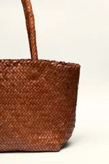 Bolso tipo tote de cuero vacuno, completamente trenzado a mano. El color es marrón oscuro, casi chocolate. Posee dos asas de hombro trenzadas.