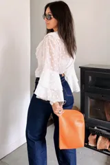 Blusa blanca con estampado de lunares, confeccionada en tela semitransparente. Presenta escote en V con volados frontales y mangas largas acampanadas con volados en los puños.