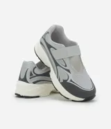 Championes de estilo híbrido entre jogging y Mary Jane, confeccionados en poliuretano. Presentan un diseño con cierre de tira adherente en el empeine, suela robusta y detalles en tonos grises y plateados.