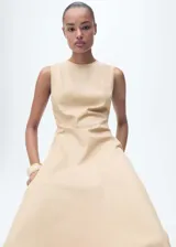 Vestido midi de corte evasé en color beige, confeccionado en una mezcla de algodón y lyocell. Presenta cuello redondo, diseño sin mangas con tirantes anchos, costuras estructuradas y bajo asimétrico con acabado deshilachado. Incluye cierre de cremallera en la parte posterior y forro interior de algodón.