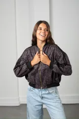 Campera tipo bomber con estampado animal print en tonos oscuros, cierre frontal con cremallera dorada, cuello, puños y ruedo en tejido elástico negro, y detalle de tres bandas laterales en las mangas.