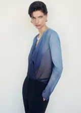 Blusa de manga larga con diseño degradado en tonos azules. Presenta un tejido fluido y semitransparente, con un elegante cuello cruzado y corte recto.