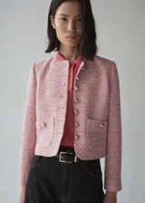 Chaqueta de tweed en tonos rosados, con cuello redondo, manga larga y cierre frontal con botones metálicos. Presenta dos bolsillos de parche en la parte delantera y diseño entallado con forro interior.