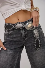 Cinto de cuero negro con diseño estilo western, compuesto por placas metálicas ovaladas con grabados y ojales metálicos decorativos. Incluye una hebilla central grande con detalle de piedra clara.