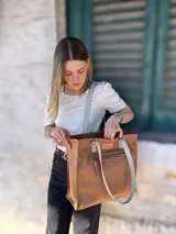 Bolso tipo tote de cuero color camel con forro de tela, doble asa corta y bolsillo frontal con cierre.