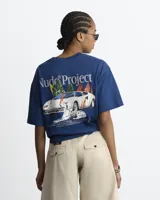Remera azul marino de manga corta de la marca Nude Project, con cuello redondo y diseño gráfico en la espalda que incluye un auto deportivo en llamas, un perro dálmata y texto descriptivo.