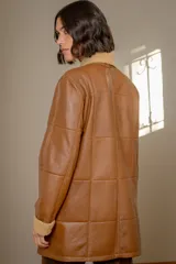 Campera de cuero negro con diseño de paneles, cuello alto y puños con forro de corderito sintético negro. Presenta cierre frontal con botones a tono.