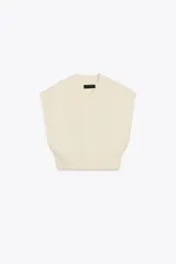 Chaleco de punto liso con escote en pico y diseño sin mangas. Presenta un corte corto con acabados en rib en el cuello, las sisas y el ruedo.