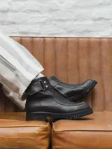 Bota corta de cuero color gris y beige, con detalle de correa marrón con hebilla y tachas plateadas. Tiene suela de goma negra y taco de madera.