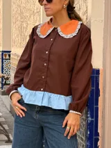 Camisa de manga larga en color marrón chocolate, con cuello redondo estilo Peter Pan en color naranja con borde a cuadros y detalle de volado en el ruedo en color celeste.