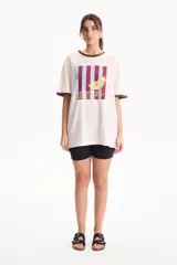 Remera de algodón blanca de manga corta, con corte suelto (loose fit) y rib en contraste marrón en el cuello y los puños. Presenta un estampado frontal rectangular con rayas verticales en tonos burdeos y celestes, superpuesto con el dibujo de una rodaja de limón amarilla y texto impreso.