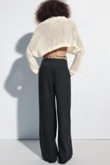 Pantalón de lino negro de tiro medio, con pernera recta, pinzas delanteras y detalle de puntilla en la cintura. Cuenta con bolsillos frontales y cierre con cremallera y botón.