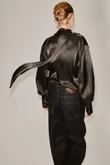Blusa de seda color marrón oscuro con estampado geométrico sutil. Presenta un diseño de cuello fluido tipo pañuelo, manga larga con puños anchos y una caída suave y elegante.
