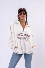 Buzo de algodón color marrón chocolate, con cuello alto y cierre frontal parcial. Presenta un estampado gráfico en el pecho con la inscripción 'NYC 1988' y detalles de texto en color blanco.