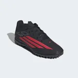 Championes de fútbol Adidas F50 Club para césped artificial, color negro con detalles en rojo y blanco. Presentan un exterior sintético liviano, lengüeta transpirable y suela de caucho con tapones diseñados para un agarre óptimo en canchas artificiales.