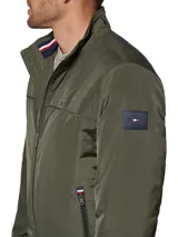 Campera bomber verde militar de poliéster, con cuello mao, cierre frontal con cremallera, dos bolsillos laterales con cremallera, puños y ruedo elásticos. Logo de Tommy Hilfiger bordado en el pecho.