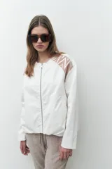 Chaqueta bomber blanca con cierre frontal, mangas largas con diseño geométrico calado en los hombros y puños elásticos.