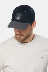 Gorro tipo gorra con visera de lona color azul, con parche tejido frontal que presenta diseño de paisaje y mar.