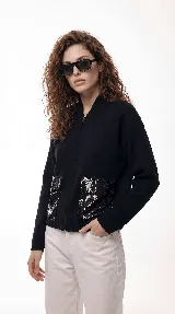 Campera de corte relajado color crema, con cierre frontal completo y cuello tipo bomber. Presenta dos bolsillos frontales destacados con apliques de lentejuelas blancas.