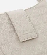 Bolso tipo baguette pequeño de color blanco hueso, con textura acolchada en patrón de rombos. Presenta un cierre principal con solapa y broche oculto, correa ajustable y un colgante rectangular decorativo en el lateral.
