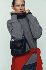 Mini bolso de mano con formato saca, confeccionado en tejido de rafia natural. Cuenta con un asa de mano ajustable en color marrón oscuro, cierre mediante cremallera metálica y detalle de doble tira frontal con terminaciones en forma de bolas.