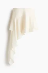 Pollera corta blanca con diseño asimétrico de dos capas de volados, donde la capa inferior se extiende formando un panel drapeado largo hacia un costado.