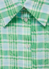 Camisa sin mangas de corte recto, confeccionada en tejido mezcla de algodón con estampado de cuadros en tonos verdes y celestes. Presenta cuello camisero y cierre frontal con botones.