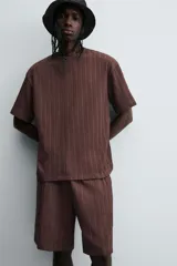 Camiseta de algodón de corte relajado (relaxed fit) color marrón oscuro, con cuello redondo y manga corta. Presenta una textura acanalada vertical tipo jacquard.