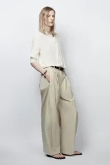 Camisa fluida de cuello redondo y manga larga con puños. Presenta un diseño con pechera frontal, cierre con botones y bajo asimétrico redondeado.