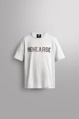 Camiseta de algodón gris melange con cuello redondo, mangas cortas y efecto lavado. Presenta un estampado de texto frontal en color oscuro con efecto desgastado.