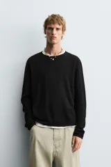 Jersey de manga larga, cuello redondo y calce relajado, color negro con efecto lavado y textura tejida.