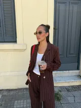 Conjunto de dos piezas compuesto por un blazer y un pantalón de corte sastrero, confeccionados en tela de algodón con estampado de rayas verticales blancas sobre fondo gris. El blazer presenta solapas clásicas y cierre frontal, mientras que el pantalón es de tiro medio y pierna recta.