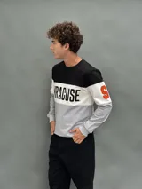 Buzo de cuello redondo con diseño de bloques de color en negro, blanco y gris. Presenta la palabra 'SYRACUSE' estampada en el frente y detalles en naranja en las mangas.