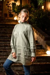 Camisa verde militar de algodón con cuello alto con volado, mangas largas con aberturas y tiras para atar, tablas en la parte inferior y cierre con tres ataduras.
