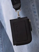 Tarjetero Rusty Runoi con cierre y correa para colgar, confeccionado en poliuretano color verde con aplique naranja y logo de la marca.