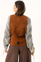 Chaleco oversize confeccionado en cuero descarne, con diseño de terminación en picos, detalle de tachas metálicas en los bordes frontales y flecos en la espalda.