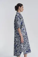 Vestido camisero midi con estampado floral en tonos azul, blanco y negro. Tiene cuello camisero, mangas 3/4 y abotonadura frontal parcial.