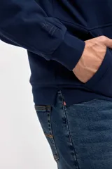 Canguro de felpa con friza, diseño con cortes en el cuerpo y bolsillos laterales integrados. Presenta capucha, puños elásticos y un pequeño detalle bordado en la manga.